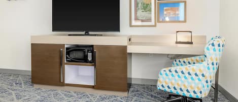 Une chambre d’hôtel moderne dotée d’un téléviseur à écran plat, d’un four à micro-ondes rangé dans un meuble, d’un tapis à motifs et d’une chaise de bureau colorée.