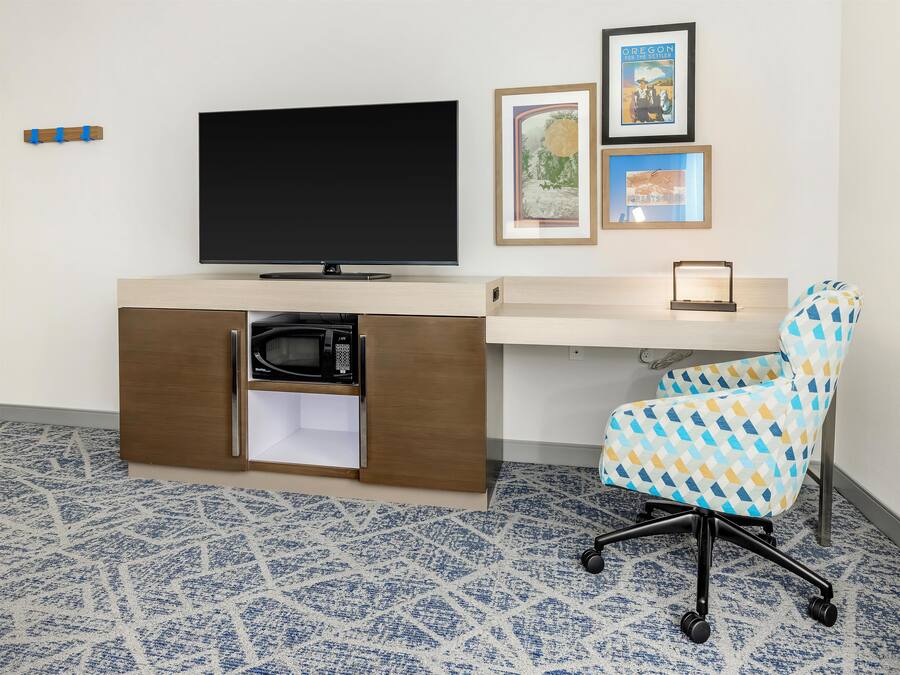 Een moderne hotelkamer met een flatscreen-tv, een magnetron in een kast, een kamerkleed met dessin en een kleurrijke bureaustoel.