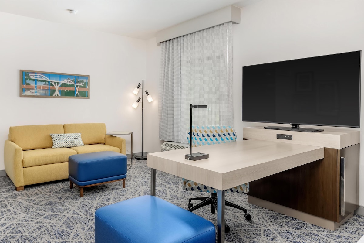 A modern hotel room with a sofa, a desk, a television, and a patterned carpet.