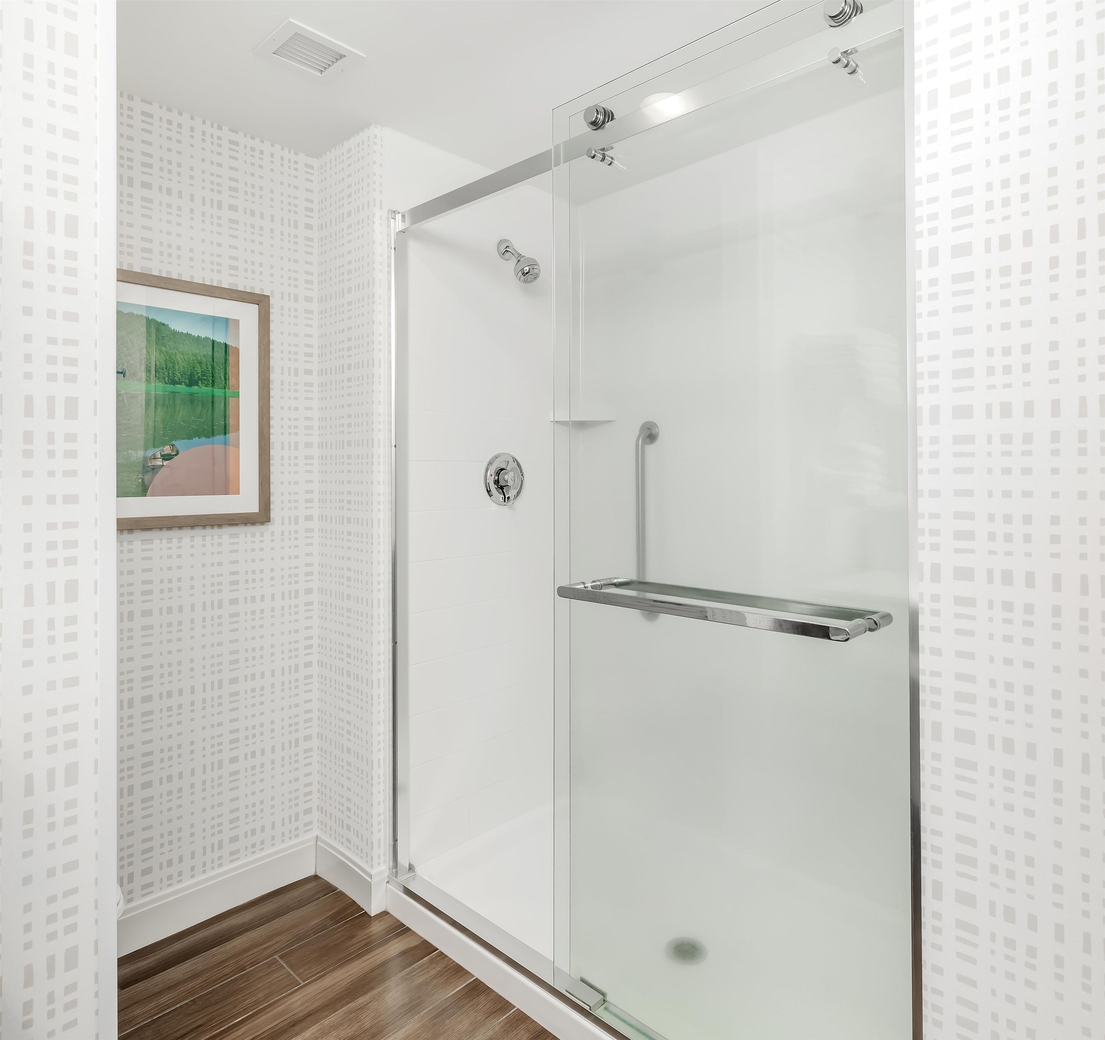 A glass-enclosed shower with a metal handle and a glass shelf.