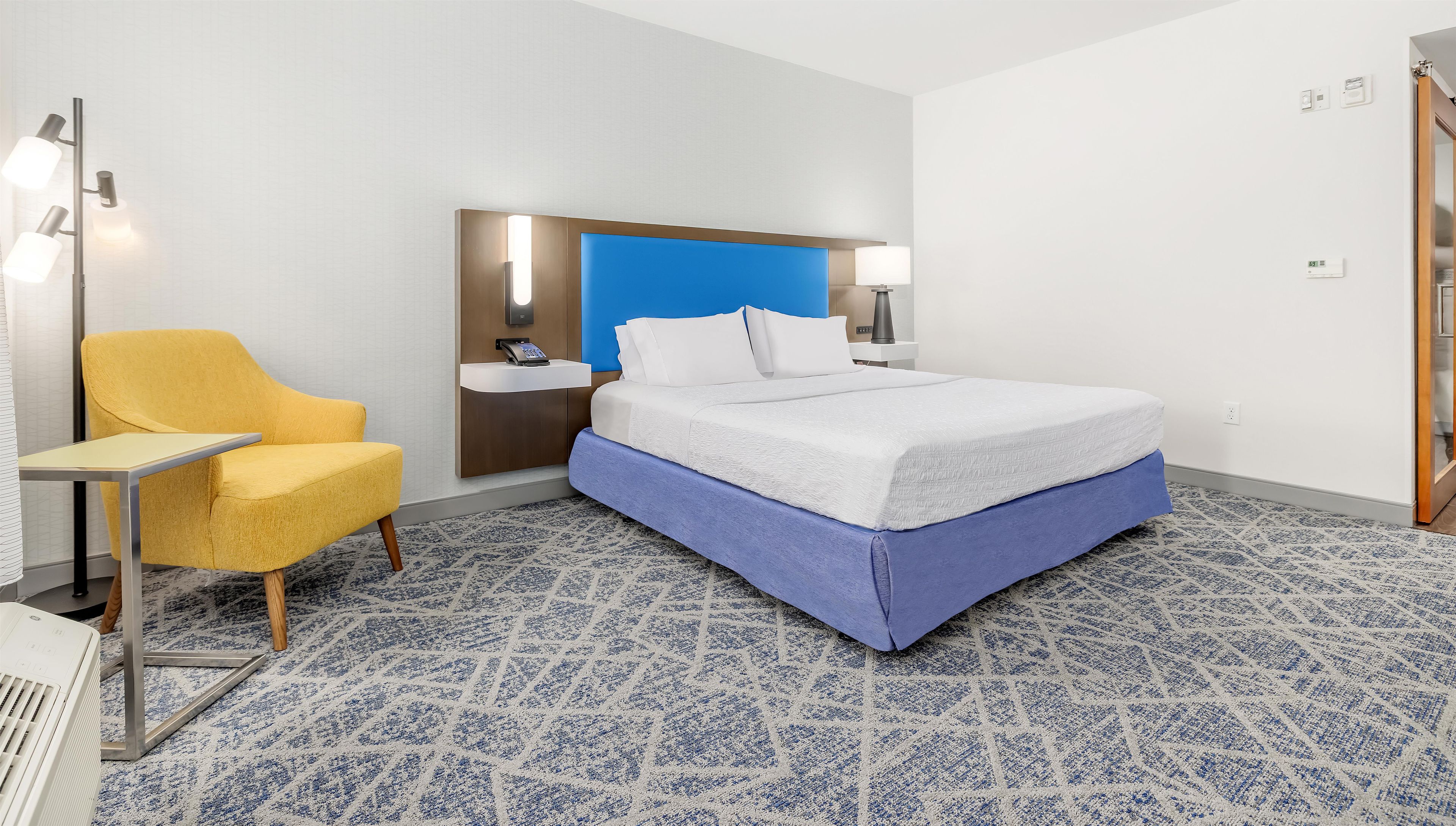 Une chambre d’hôtel équipée d’un lit, d’un bureau, d’une chaise, d’une table de chevet et d’un téléphone fixé au mur.