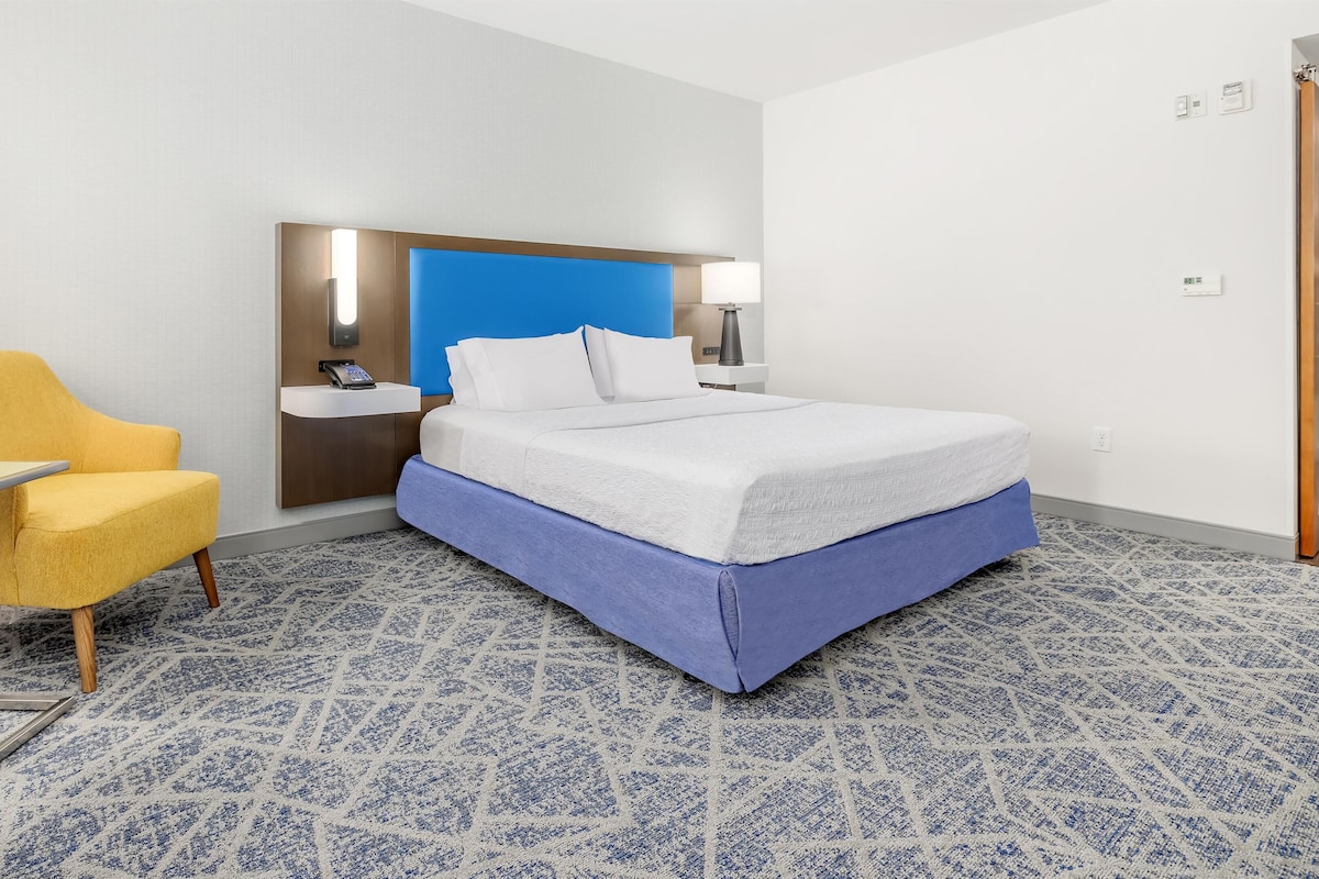 A hotel room with a bed, a desk, a chair, a bedside table, a wall-mounted phone, and a blue accent wall.