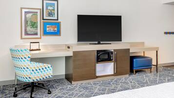 A hotel room with a desk, a television, a chair, and a bed.