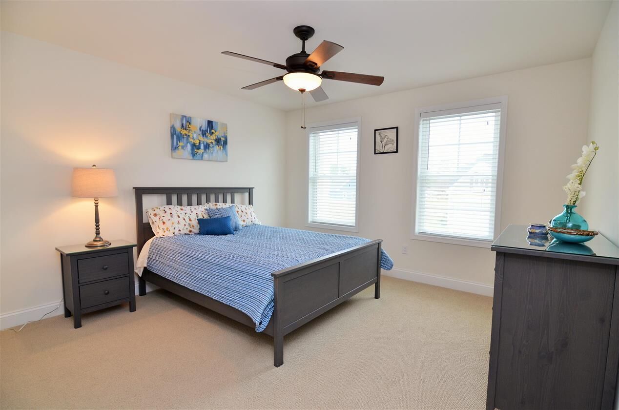 A bedroom with a bed, nightstand, lamp, ceiling fan, and a dresser.