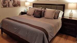 Quarto bem arrumado com uma cama grande, duas mesinhas de cabeceira, encosto de cama e um quadro na parede.