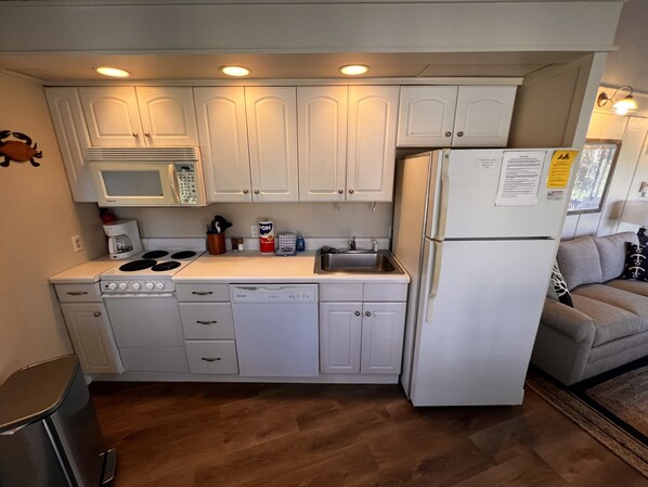 A compact kitchen with white cabinets, a microwave, stove, sink, and dishwasher.