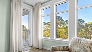 A room with a large window, a sofa, and a door leading to a balcony. - Great Bay Views, Steps to Baytowne Wharf, Balcony, Beach Tram, Pool, Hot Tub. (Miramar Beach)