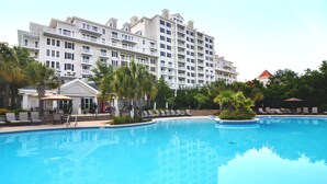 A hotel with a large pool, multiple balconies, and palm trees. - Great Bay Views, Steps to Baytowne Wharf, Balcony, Beach Tram, Pool, Hot Tub. (Miramar Beach)