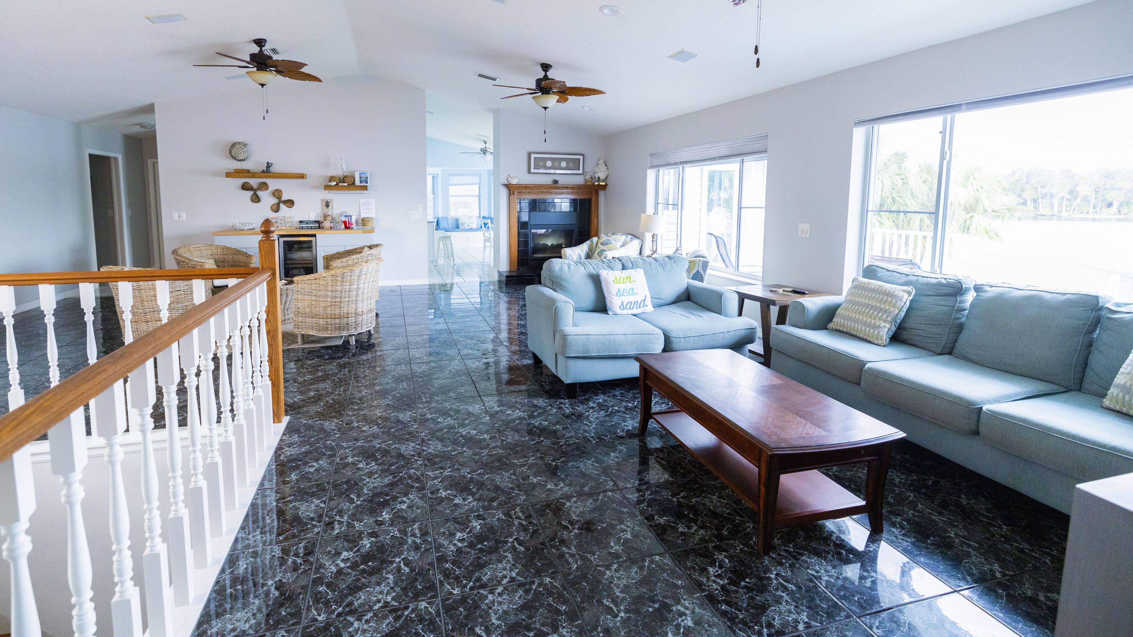 A spacious living area with a marble floor, a light blue sofa, a wooden coffee table, wicker chairs, and a fireplace.