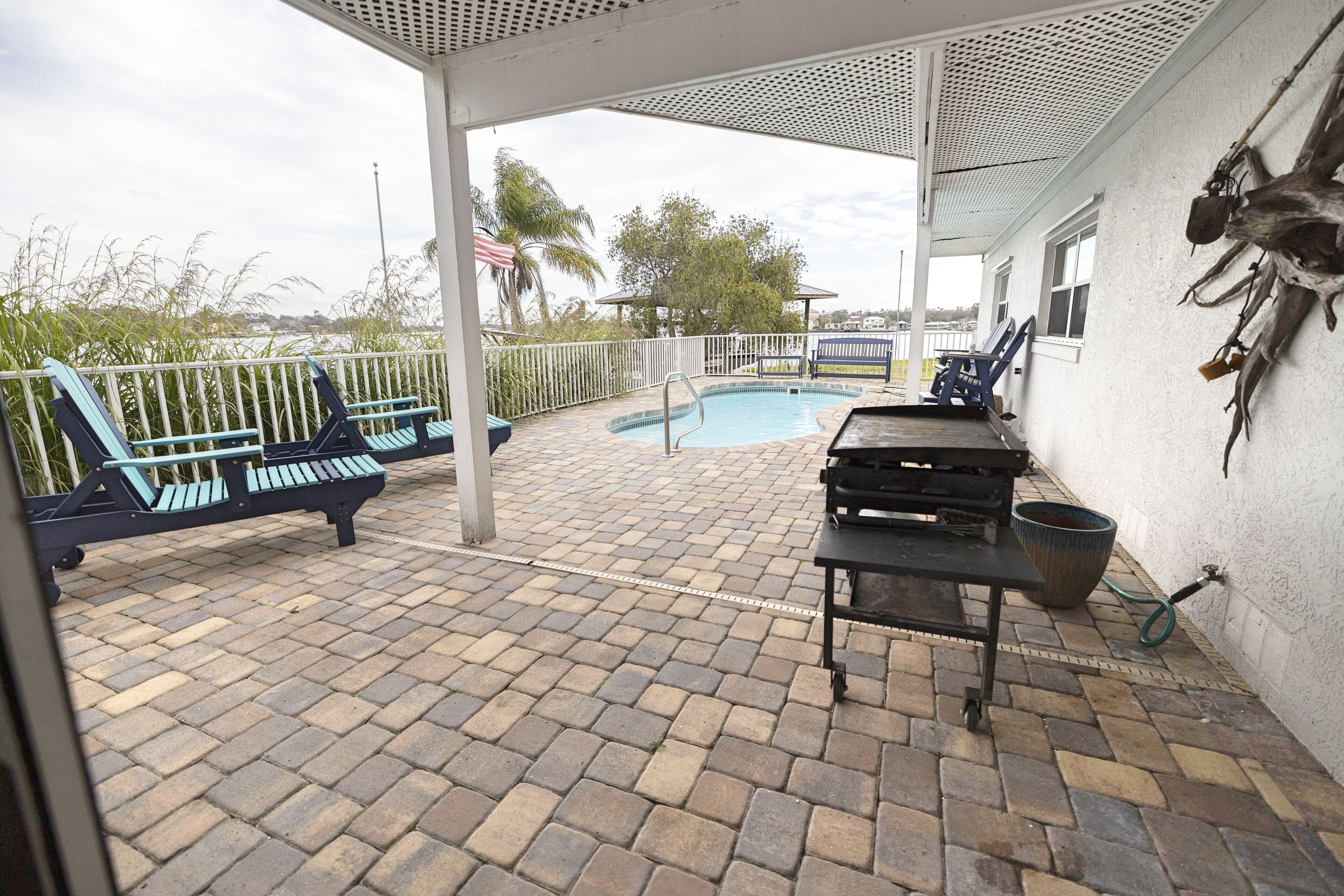 Ein überdachter Patio-Bereich mit Pool, Liegestühlen und Grill.