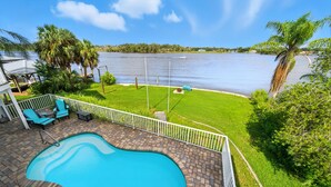 A swimming pool with a view of a lake, surrounded by a deck with chairs and a fence. - Million dollar house on main river w/ million dollar view! Pool, Dock, Kayaks. (Crystal River)