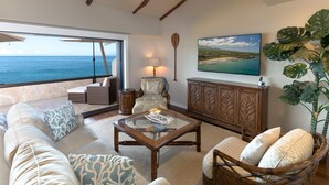 A spacious living area with a large glass coffee table, comfortable seating, a wooden cabinet, and a view of the ocean. - Beachfront Condo B303 - December 13-27 Still Available! (Kihei)