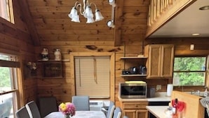 A wooden cabin interior with a dining table, chairs, a kitchen area, and a hanging light fixture. - Spacious Log Cabin Perfect for Families and Pets (Glover)
