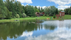A lakeside property with a wooden cabin, a large house, and a small playhouse. - Spacious Log Cabin Perfect for Families and Pets (Glover)