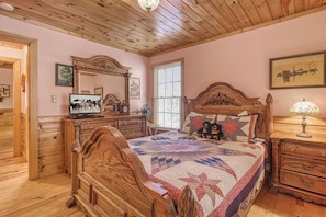 Ein gemütliches Schlafzimmer mit einem hölzernen Bett, einer Kommode, einem Schminktisch mit Spiegel und einem Fernseher auf einem Holzschrank.
