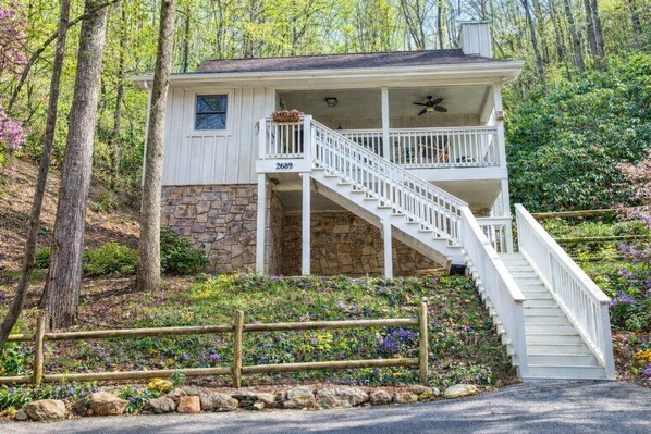 A two-story house with a stone foundation, a white exterior, and a wooden staircase leading to the upper floor.