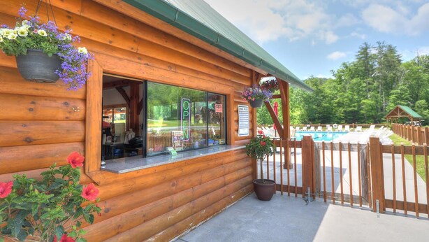 Eine Holzhütte mit Glastür, einer kleinen Sitzgelegenheit im Freien und Blick auf einen Swimmingpool.