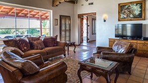 A spacious living room with leather sofas, a glass coffee table, and a television on a wooden cabinet.