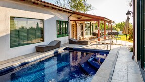 A swimming pool with a pergola and lounge chairs, a covered patio area, and a lamp post.