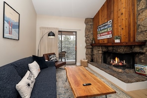 Una sala de estar con sofá, una mesa de centro, chimenea y vistas a través de un ventanal.