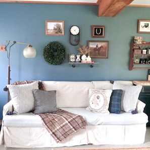 A living room with a white sofa, a clock, framed pictures, and a shelf with decorative items.