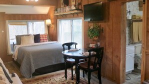 A cozy room with a bed, a dining table with chairs, a ceiling fan, and a TV mounted on the wall.