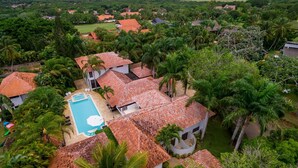 Vista aérea de una zona residencial con casas de techo rojo, rodeada de abundante vegetación y palmeras.