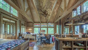 A rustic cabin interior with a large bed, a dining area, and a kitchen with wooden shelves. - TREE HOUSE on Little Peak Creek Farm! (Jefferson)