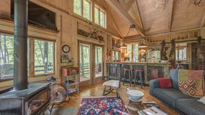 A cozy cabin interior with a wood-burning stove, a dining area, and a living room with a sofa and a rug. - TREE HOUSE on Little Peak Creek Farm! (Jefferson)