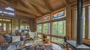 A cozy cabin interior with wooden walls, large windows, a fireplace, and a comfortable seating area. - TREE HOUSE on Little Peak Creek Farm! (Jefferson)