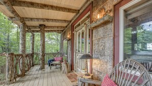 A wooden deck with rustic furniture, a welcome mat, and a stone wall. - TREE HOUSE on Little Peak Creek Farm! (Jefferson)