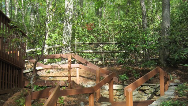 Una escalera de madera con muros de piedra, rodeada de un área boscosa.