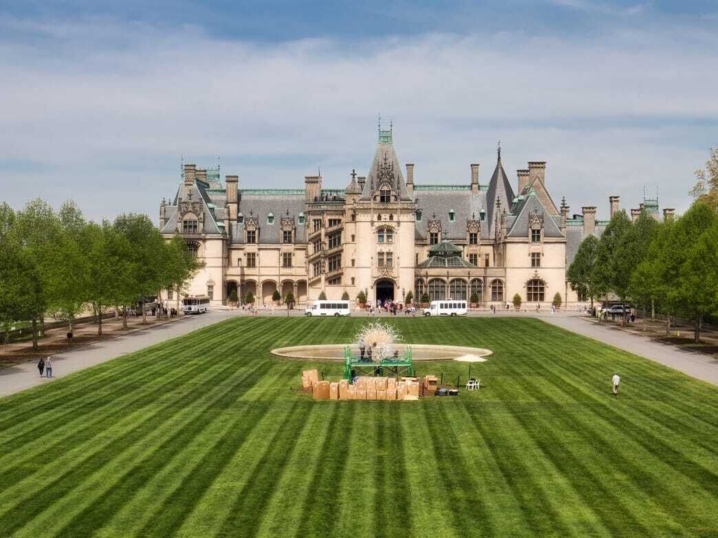 A large, historic building with a symmetrical facade, a central courtyard with a fountain, and a well-maintained lawn.