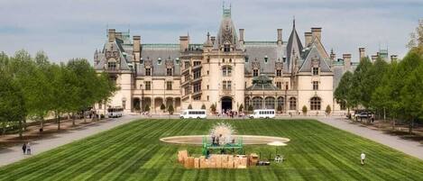 A large, historic building with a symmetrical facade, a central courtyard with a fountain, and a well-maintained lawn.