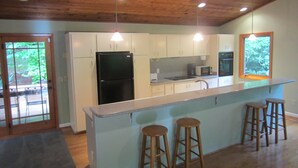 Una cocina moderna con techo de madera, armarios blancos, un refrigerador negro, un microondas y una isla grande con taburetes.