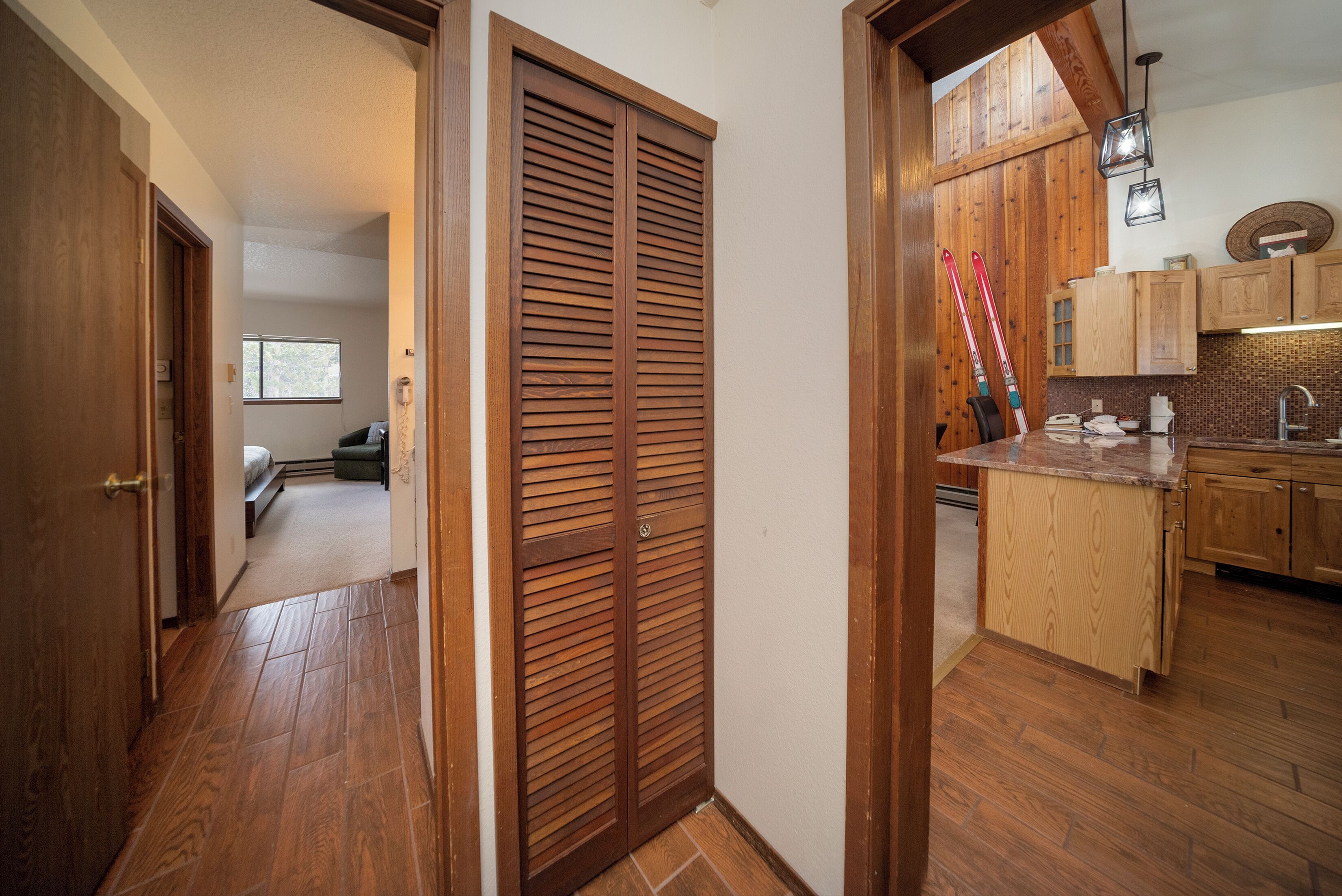 A hallway with wooden flooring leading to a kitchen area with wooden cabinets and a countertop.