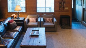 Ein gemütliches Loft-Wohnzimmer mit hoher Decke, Holzbalken, einem großen Chandelier aus Geweihen, Ledersofas, einem Couchtisch und einem Kamin.