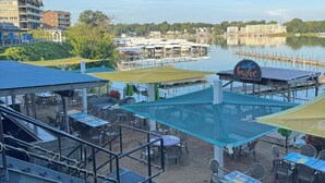 An outdoor dining area with tables and chairs, a pool, and a view of a lake and buildings in the background.