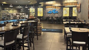 A restaurant interior with high ceilings, exposed beams, and a mix of hanging and pendant lighting. Tables and chairs are arranged for dining.