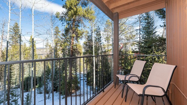 A wooden deck with two chairs and a metal railing overlooking a snowy landscape with trees.