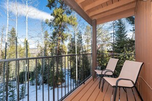 A wooden deck with two chairs and a metal railing, overlooking a snowy forest.
