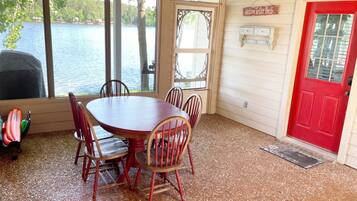 A dining area with a round table and six chairs, a red door, and a view of a lake through large windows.