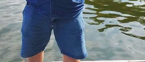 A person holding a fish on a wooden dock with a boat and fishing gear in the background.