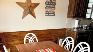 Une table à manger en bois, des chaises blanches, une décoration en forme d’étoile au mur et un tapis coloré.