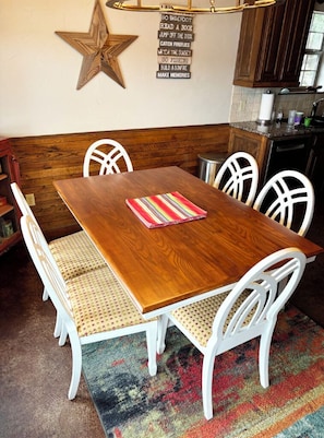 Une table à manger en bois, des chaises blanches, une décoration en forme d’étoile au mur et un tapis coloré.