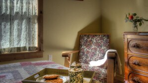 Um quarto acolhedor com cômoda de madeira, poltrona estampada e colcha acolchoada.