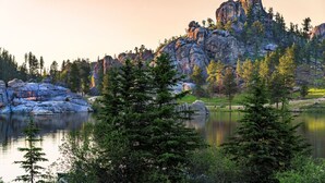Paisagem natural com um lago, falésias rochosas e árvores coníferas.