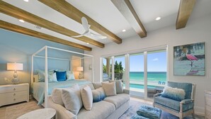A bedroom with a four-poster bed, a sitting area with a sofa and ottomans, and a view of the ocean through large sliding doors. - SEA HIS LOVE: Destiny's Gulf Front Luxury Retreat: Infinity Pool, Elevator, Daily Maid Service! (Destin)