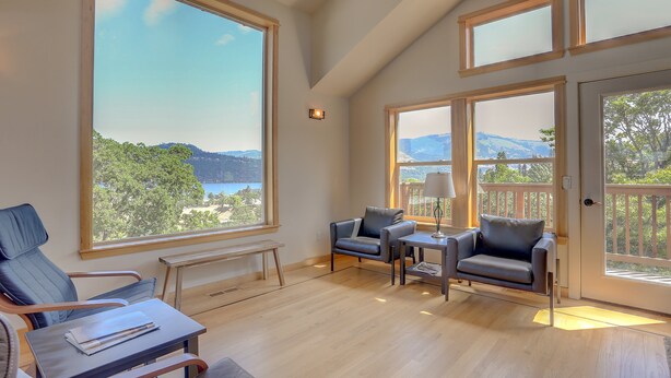 Amplia habitación con ventanas grandes que ofrecen vistas al exterior. Cuenta con un área de descanso con un banco y dos sillas.