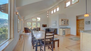 Un comedor amplio con una larga mesa y sillas de madera, una cocina con armarios de madera y ventanas grandes que ofrecen vistas al exterior.